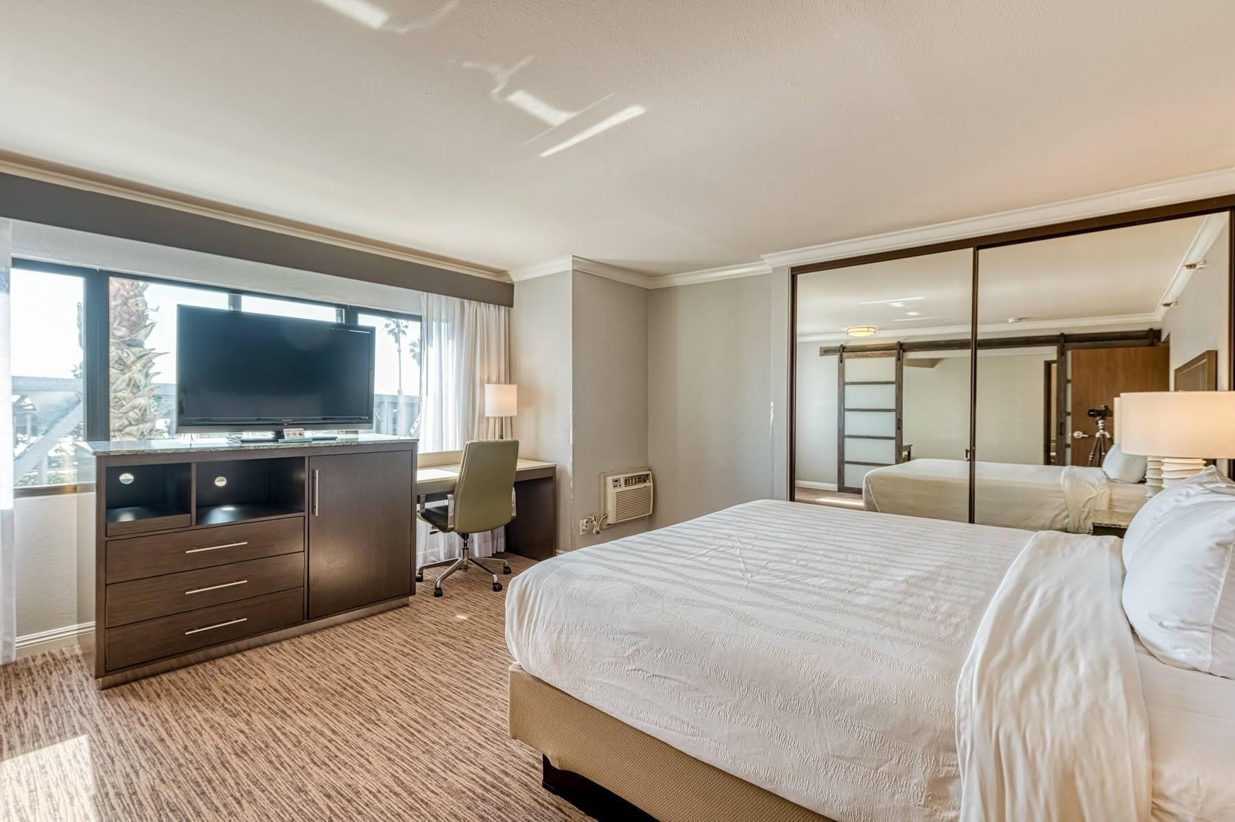 A hotel room with a bed, a desk with a computer, a TV, and a large window.