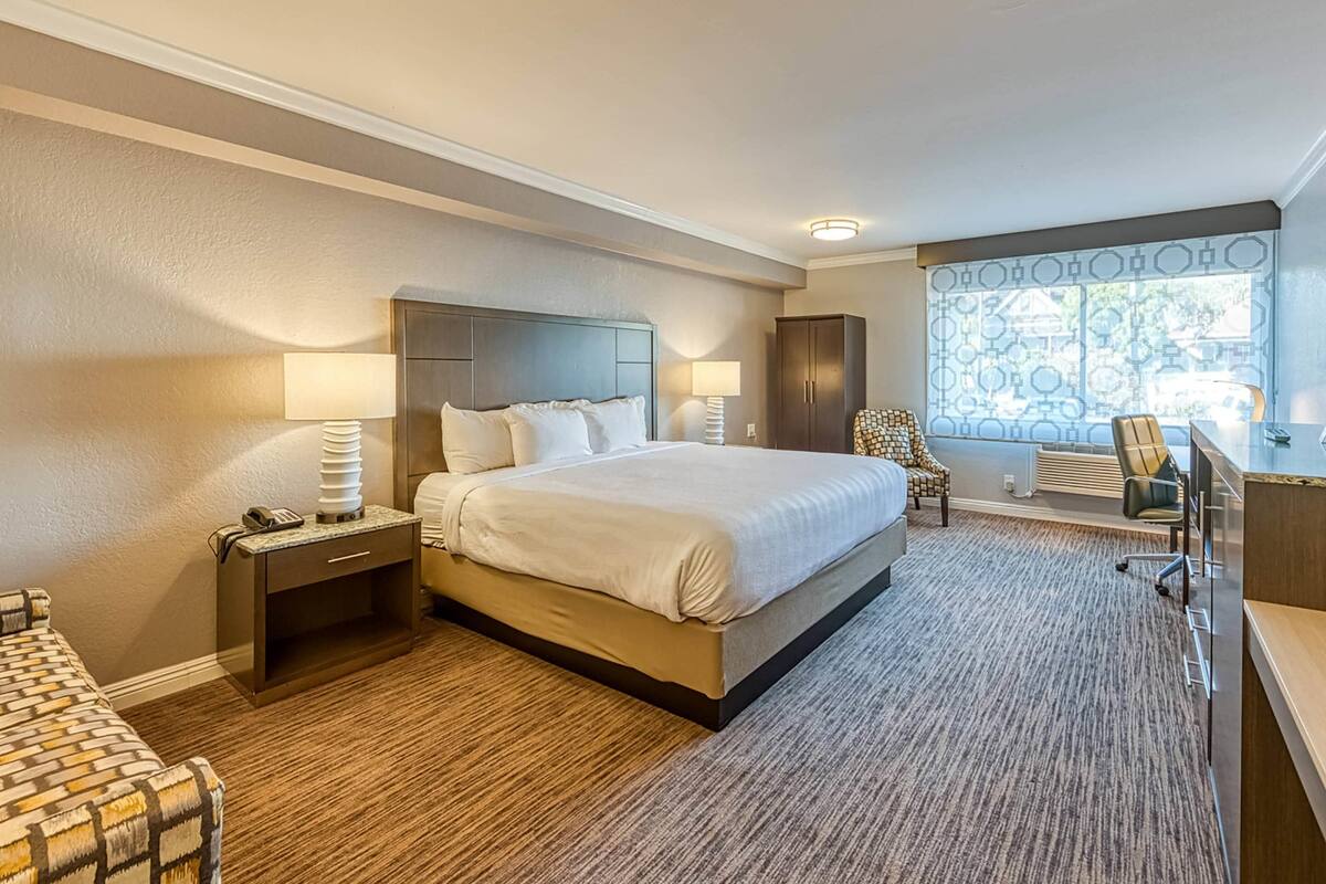 A hotel room with a large bed, bedside tables, a desk, and a chair.