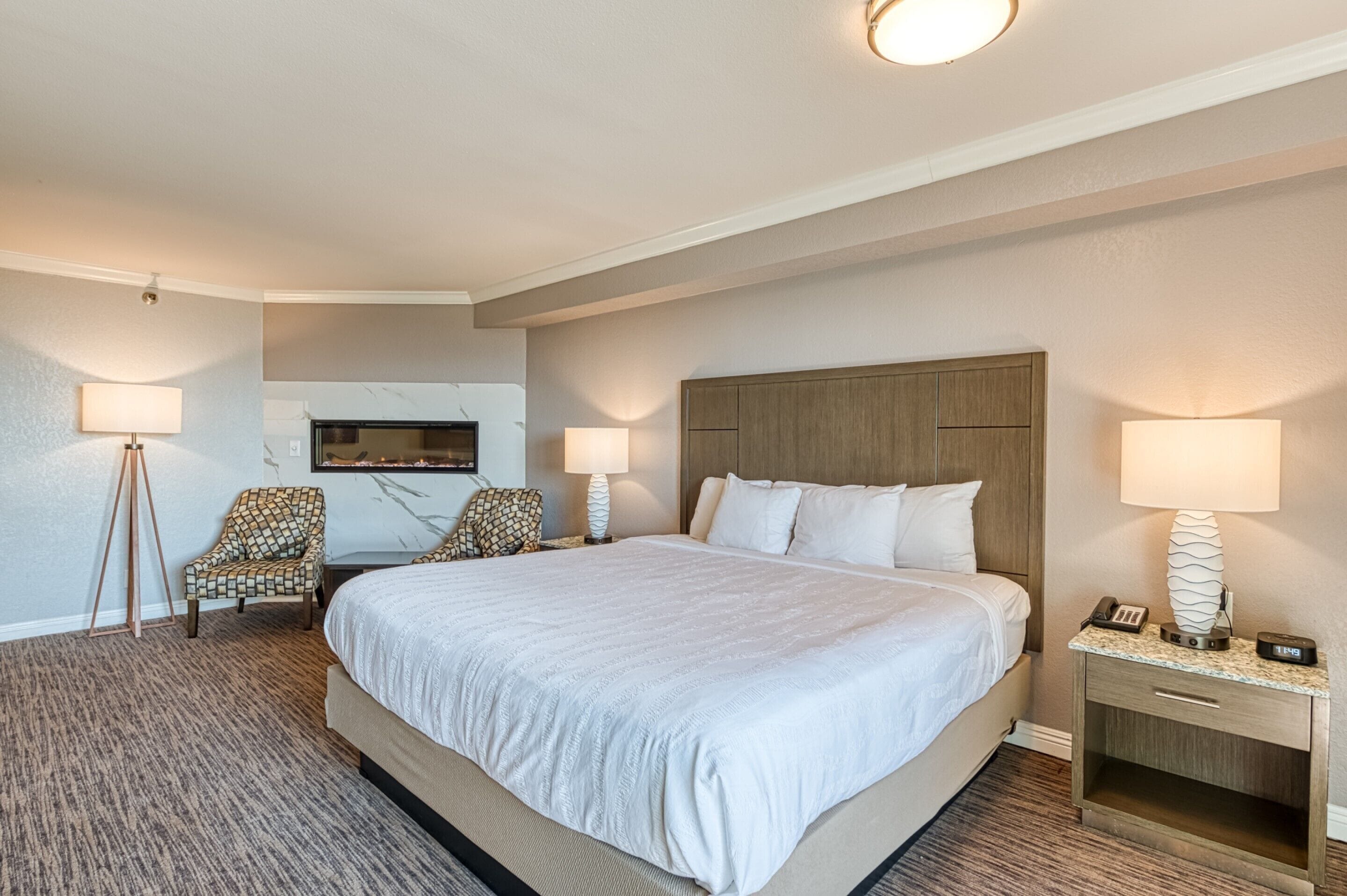 A hotel room with a large bed, two chairs, a desk with a lamp, and a TV mounted on the wall.