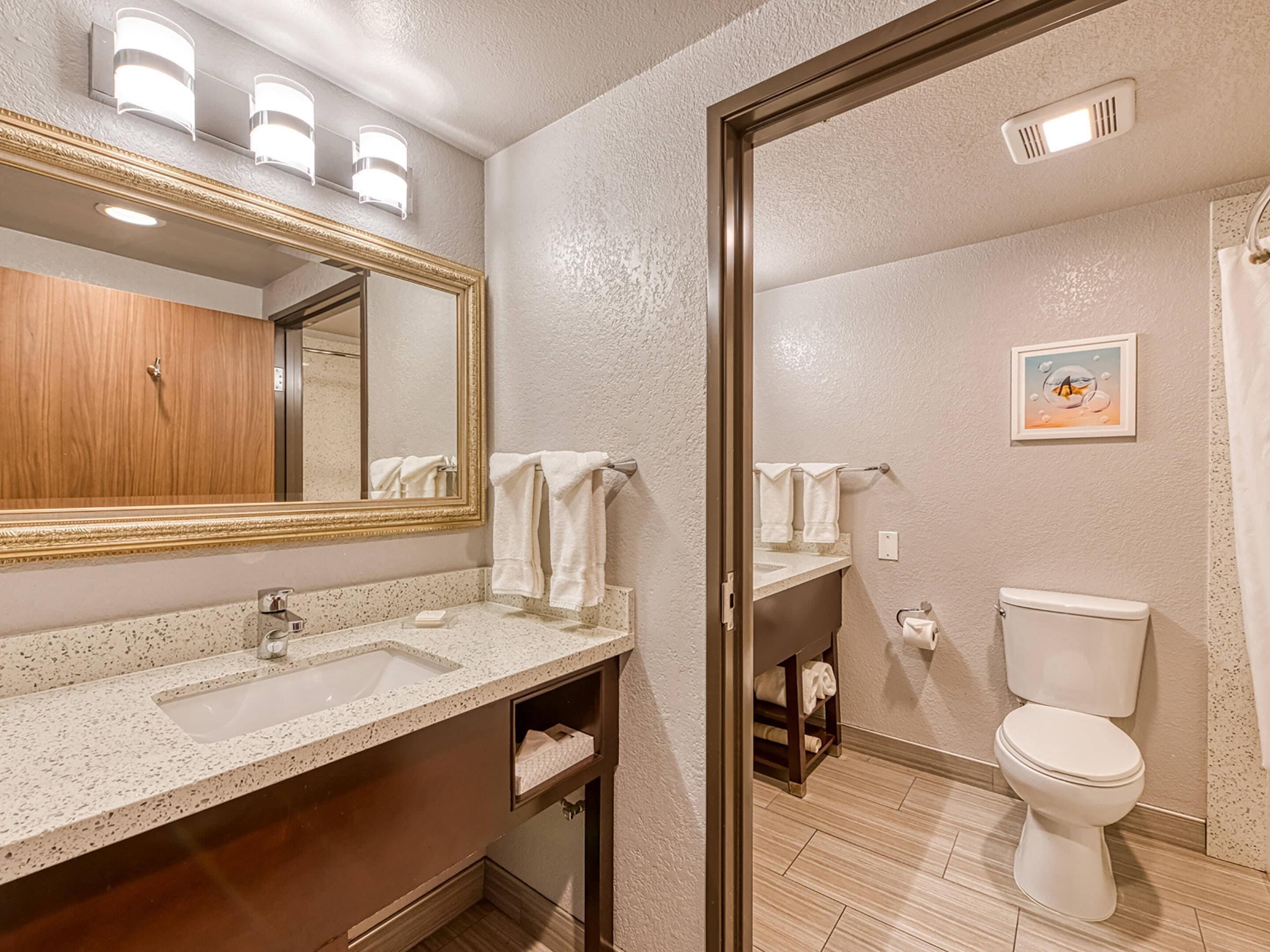 A bathroom with a large mirror, a sink, a toilet, and a shower area.