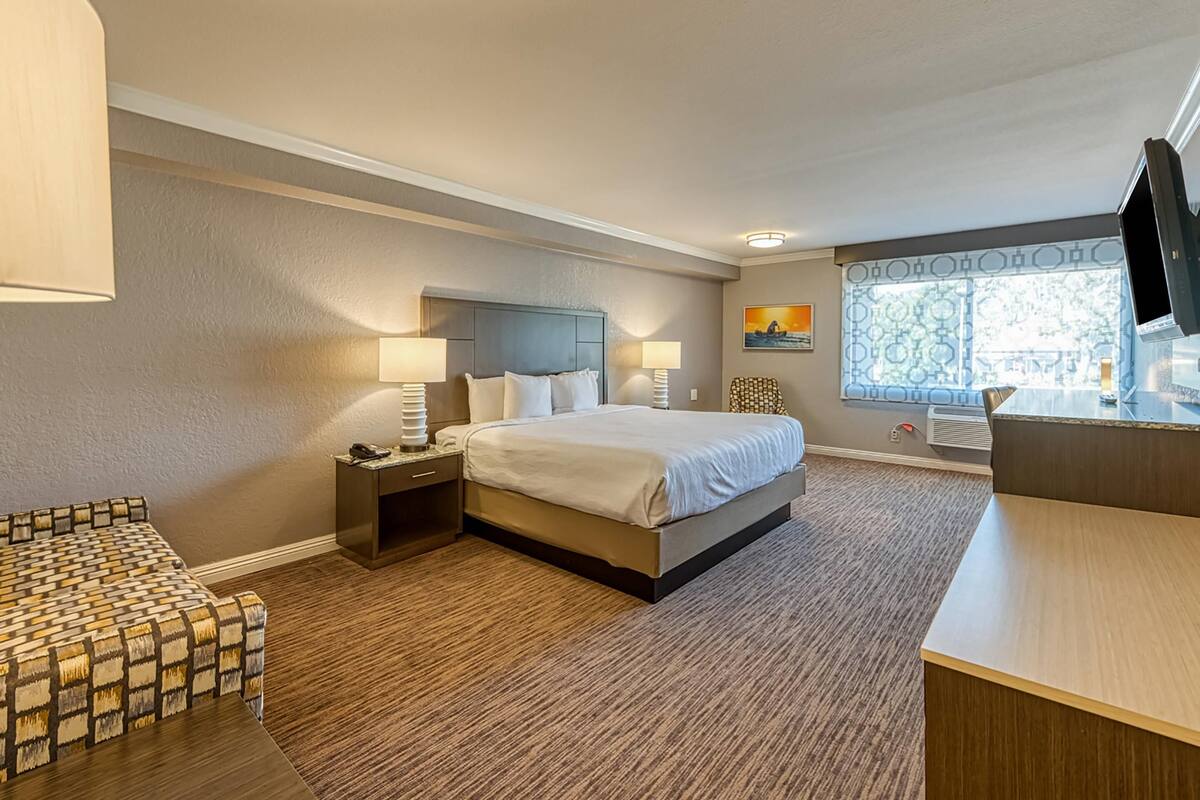 A hotel room with a bed, bedside tables, a desk, and a television.