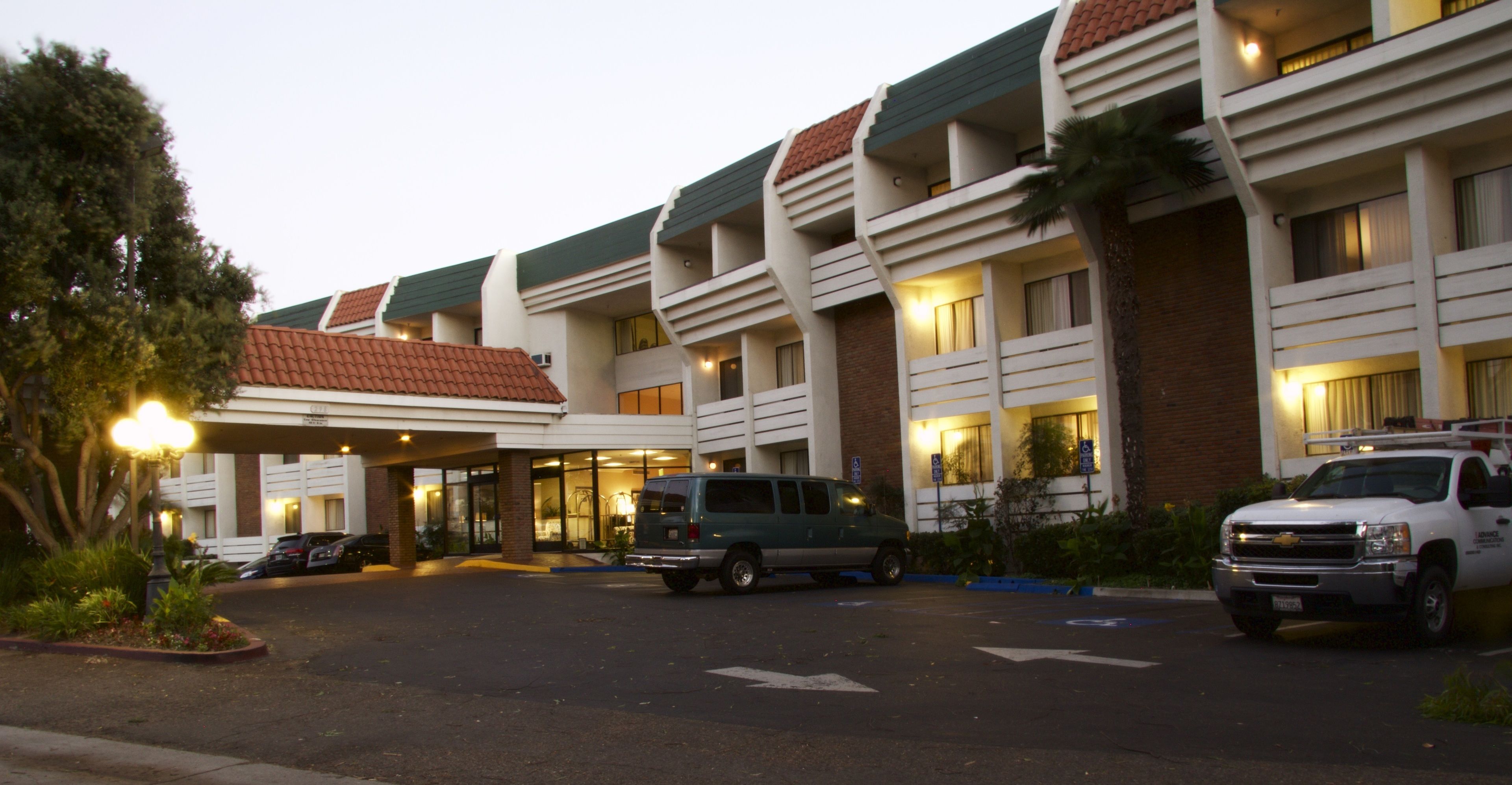 A hotel with a modern design, featuring a covered entrance, multiple floors, and a parking area with vehicles.