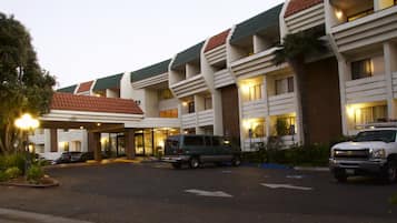 A hotel with a modern design, featuring a covered entrance, multiple floors, and a parking area with vehicles.