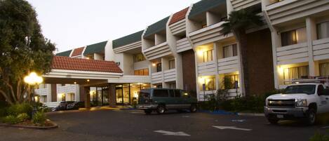 Un hotel de diseño moderno, con un acceso cubierto, varios pisos y un estacionamiento con vehículos.