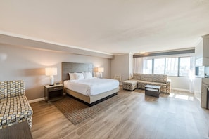 Habitación de hotel con una cama grande, dos mesitas de noche con lámparas, un sofá, una pequeña mesa y un televisor.