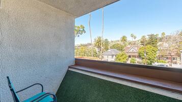 A balcony with a view of a residential area, a green artificial turf floor, and a metal bench.