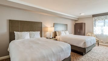 A hotel room with two beds, a nightstand, a lamp, a wardrobe, and a patterned carpet.