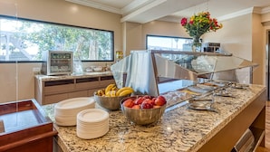 A buffet setup with fruits, plates, and a beverage dispenser.