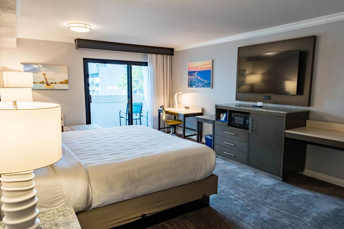 A hotel room with a bed, desk, TV, and a view of the outdoors.