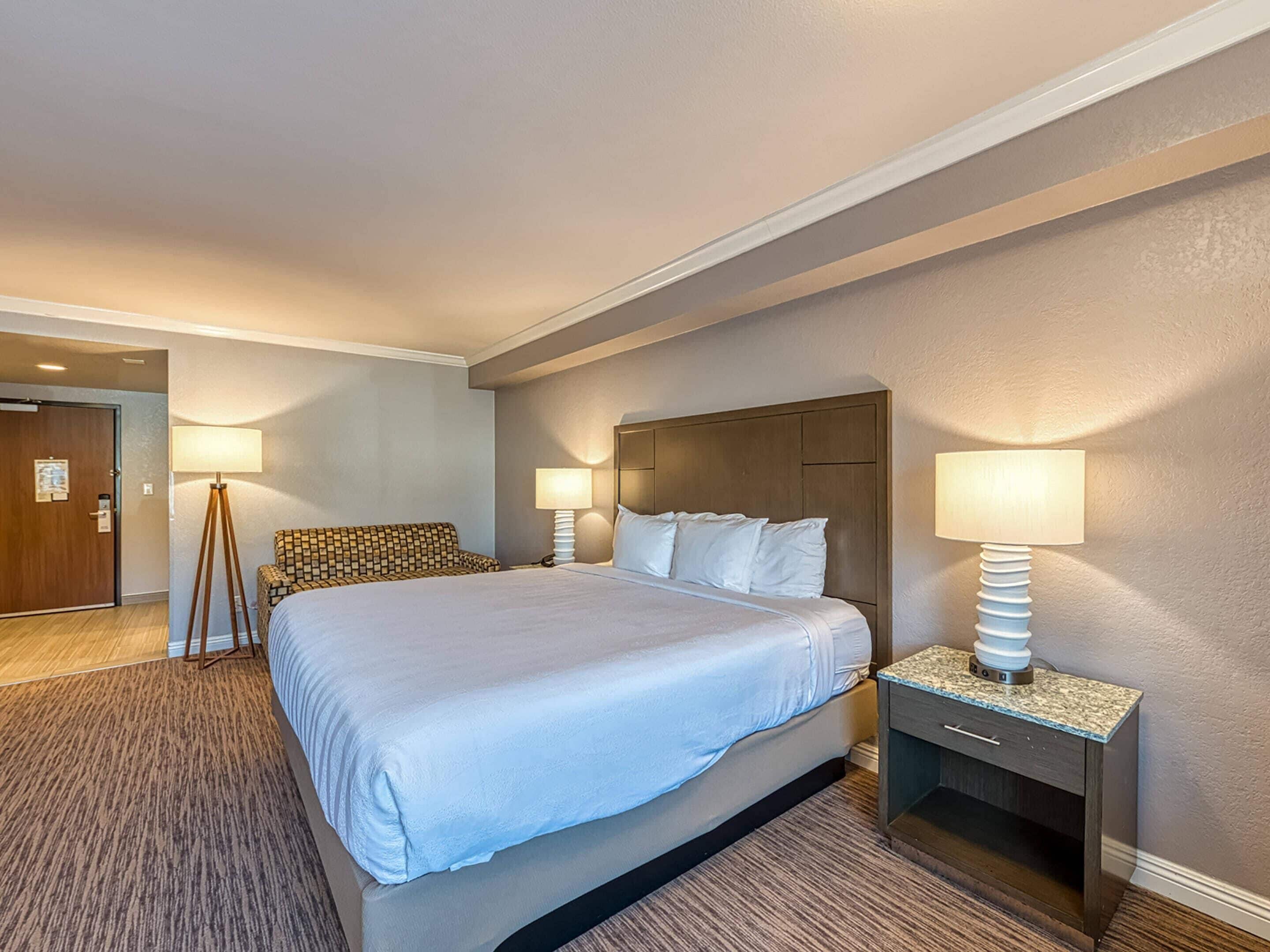 A hotel room with a large bed, two bedside tables, a headboard, and a door.