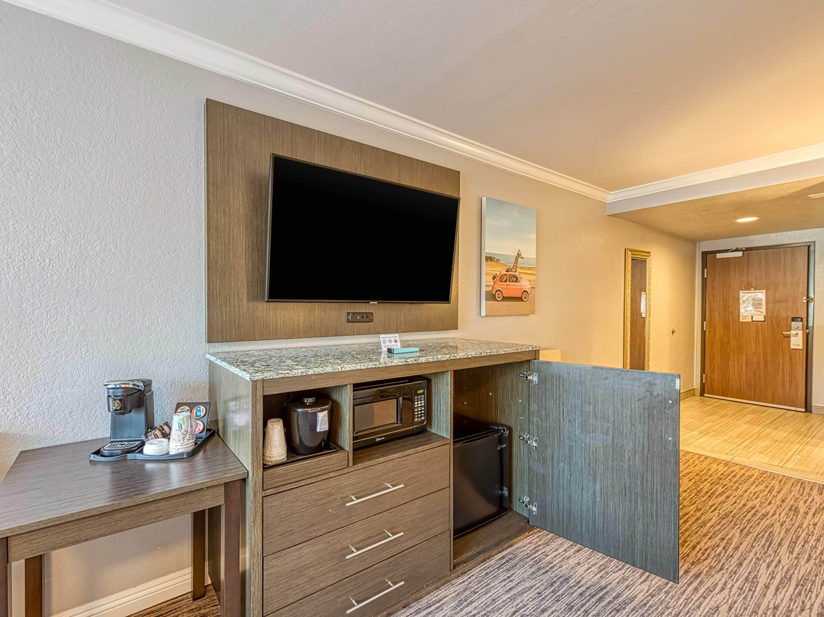 Une chambre d’hôtel équipée d’un téléviseur à écran plat fixé au-dessus d’un meuble en bois, d’une machine à café et d’un petit réfrigérateur.