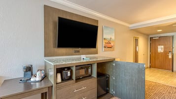 Une chambre d’hôtel équipée d’un téléviseur à écran plat fixé au-dessus d’un meuble en bois, d’une machine à café et d’un petit réfrigérateur.