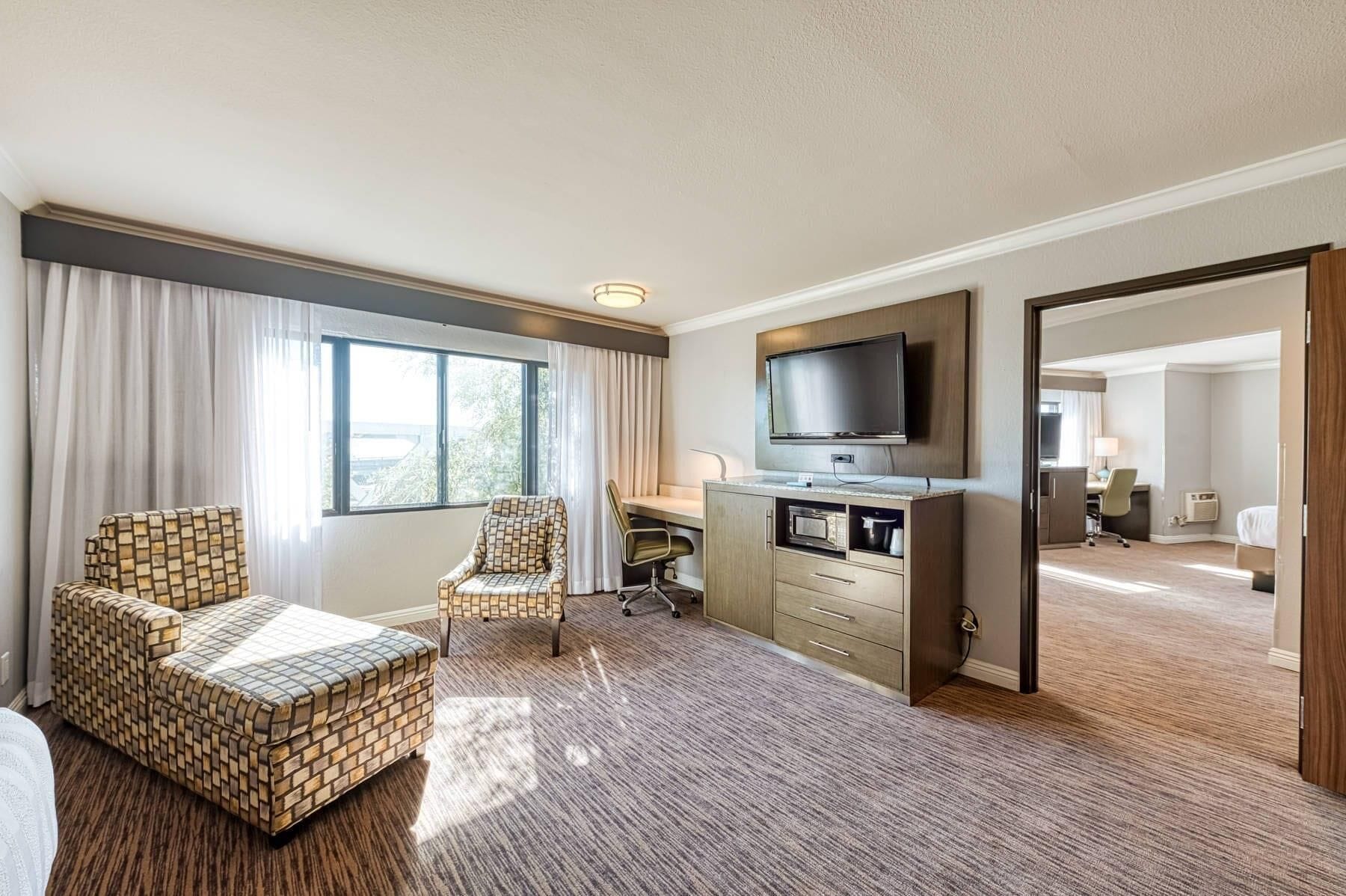 Une chambre d’hôtel avec une grande fenêtre, une télévision, un bureau, une chaise et un lit.