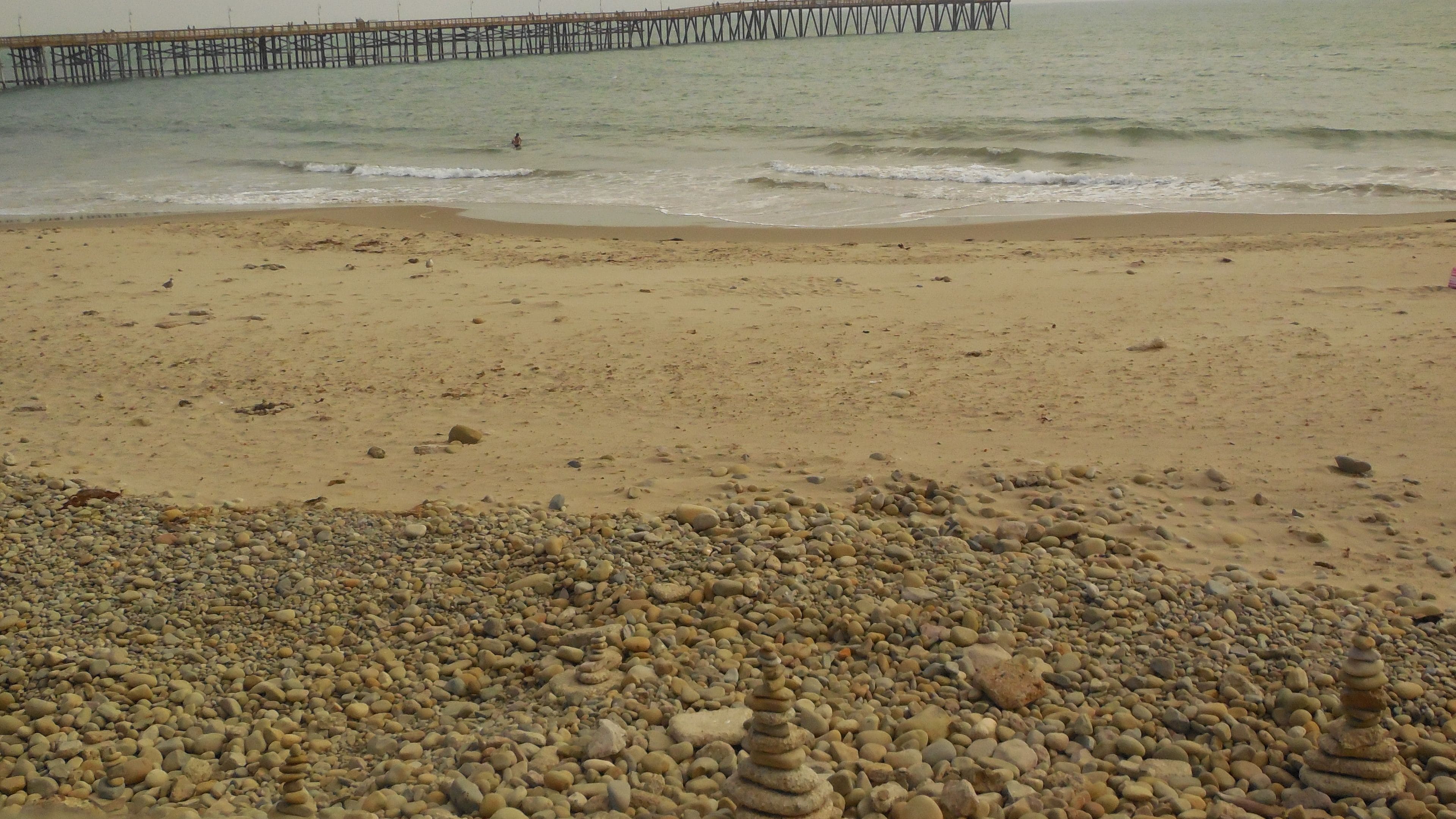 Ein Strand mit Kieselsteinen und einem hölzernen Steg im Hintergrund.