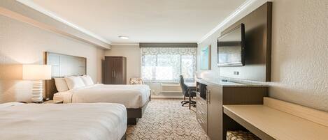 A hotel room with two beds, a desk, a TV, and a window with patterned curtains.