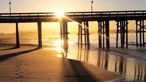 A pier extending over a beach with the sun setting in the background.