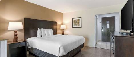 Une chambre d’hôtel comprenant un lit, des lampes de chevet, une télévision, un bureau et une porte donnant accès à une salle de bain.