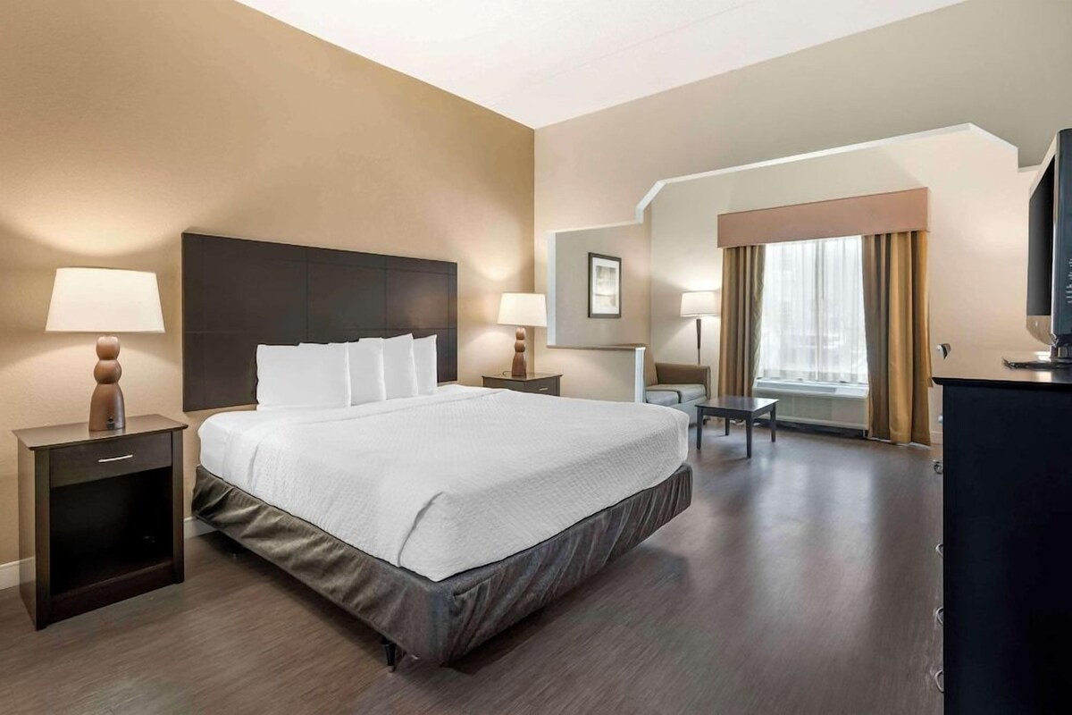 A hotel room with a large bed, bedside tables with lamps, a desk with a chair, and a television.