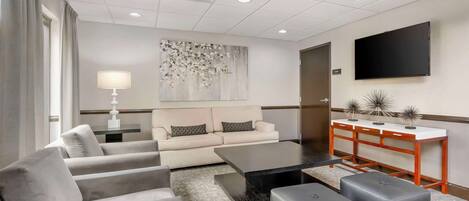 A modern hotel room with a sofa, ottomans, a coffee table, a TV, and a decorative wall piece.
