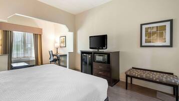 Quarto de hotel com uma cama grande, uma escrivaninha com cadeira, televisão, micro-ondas e um banco.
