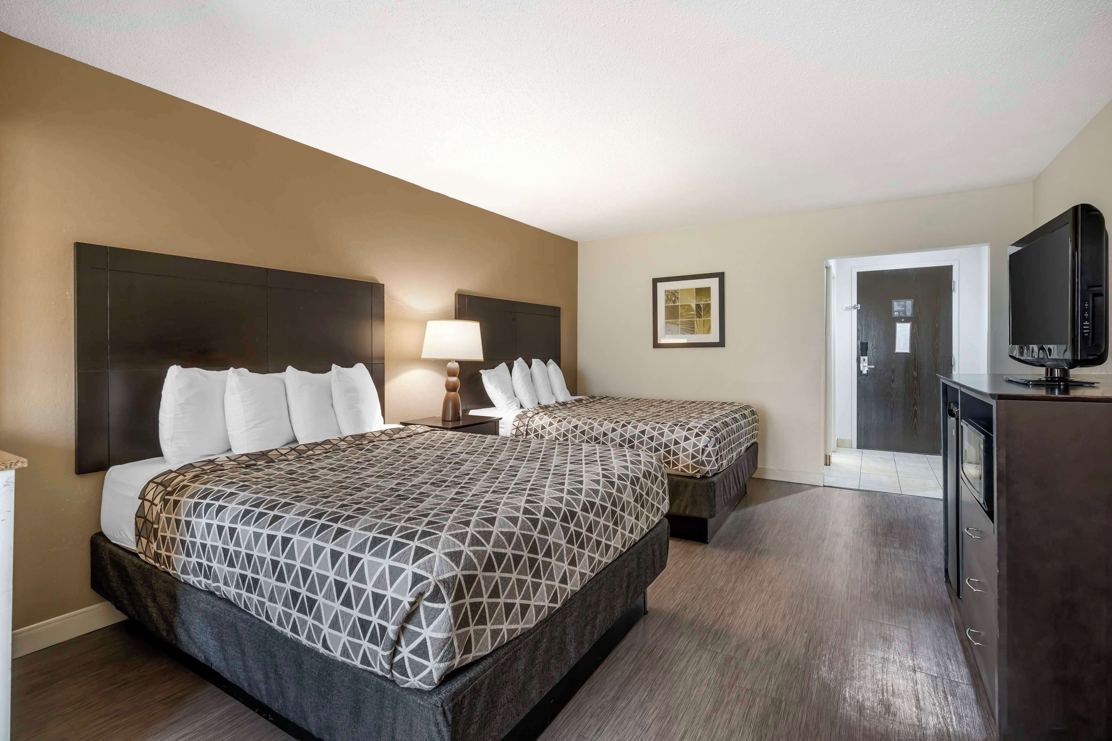 A hotel room with two beds, a TV, a desk, and a door leading to a bathroom.