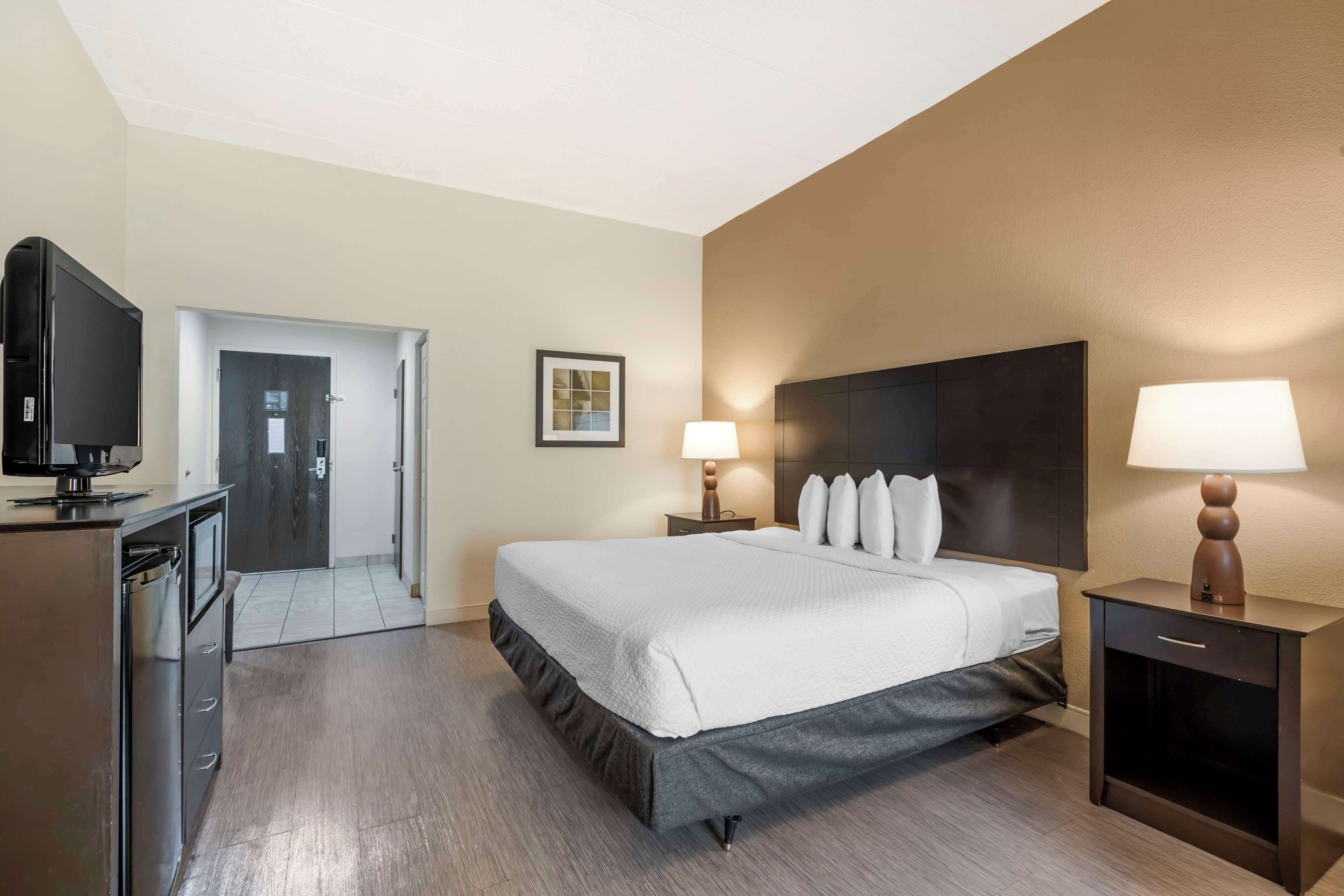 Een hotelkamer met een bed, nachtkastjes, een televisie en een deur naar een andere kamer.
