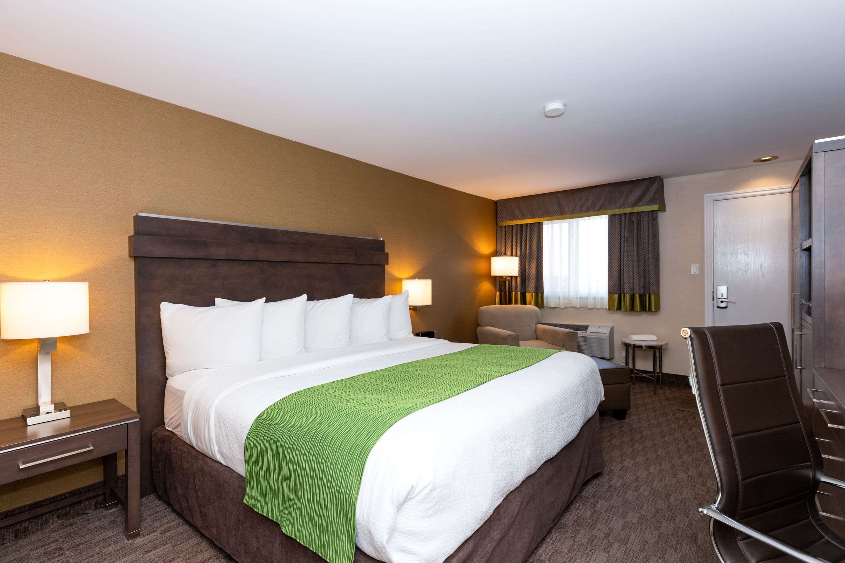 A hotel room with a large bed, two bedside lamps, a chair, a desk, and a wardrobe.