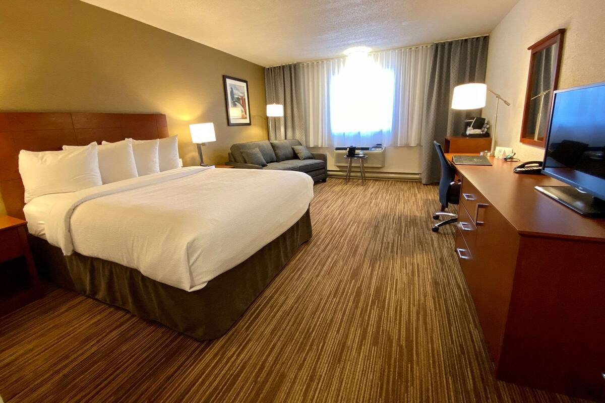 A hotel room with a large bed, a desk with a computer, a chair, and a TV.