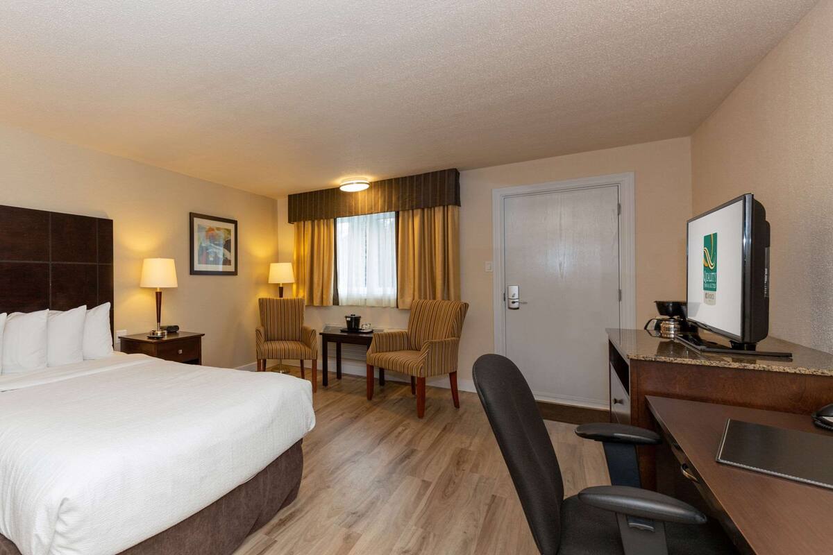 A hotel room with a large bed, a desk with a computer, two chairs, a small table, and a television.