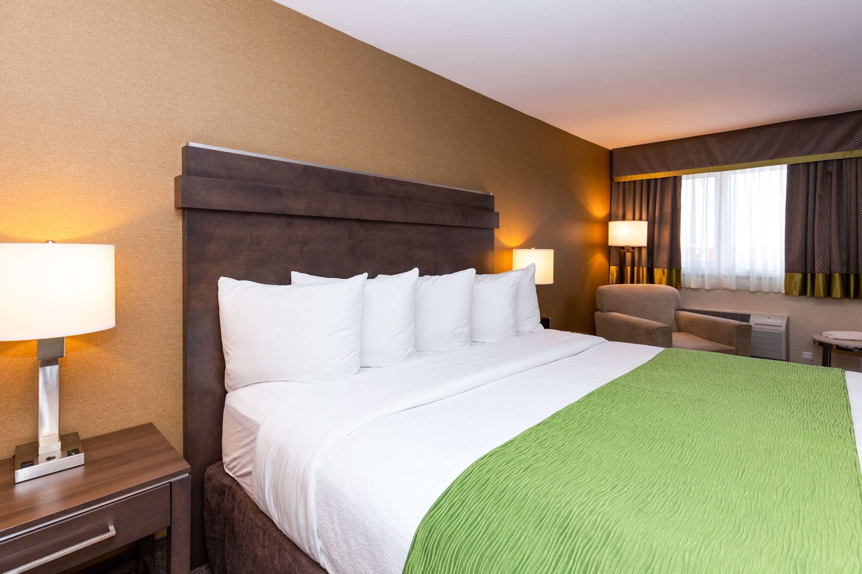 A hotel room with a large bed, two bedside tables, a green throw blanket, and two lamps.