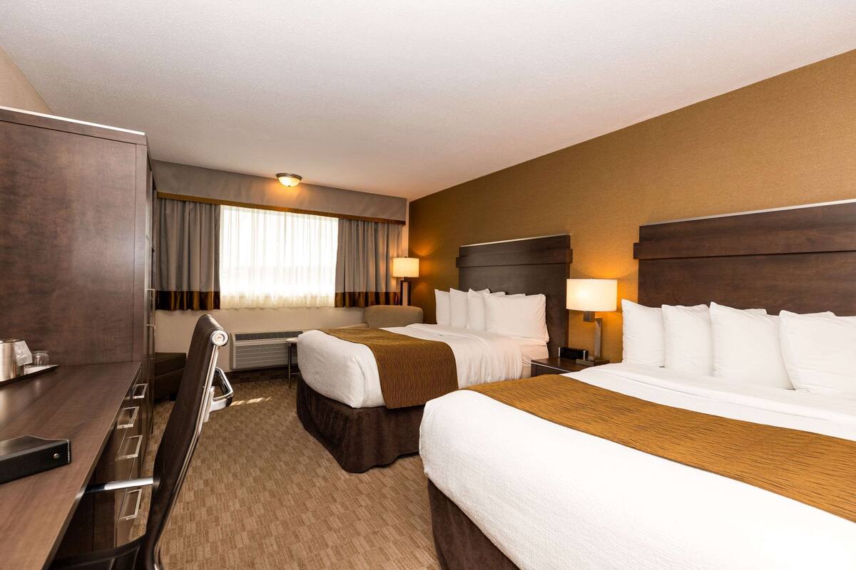 A hotel room with two beds, a desk, and a chair.