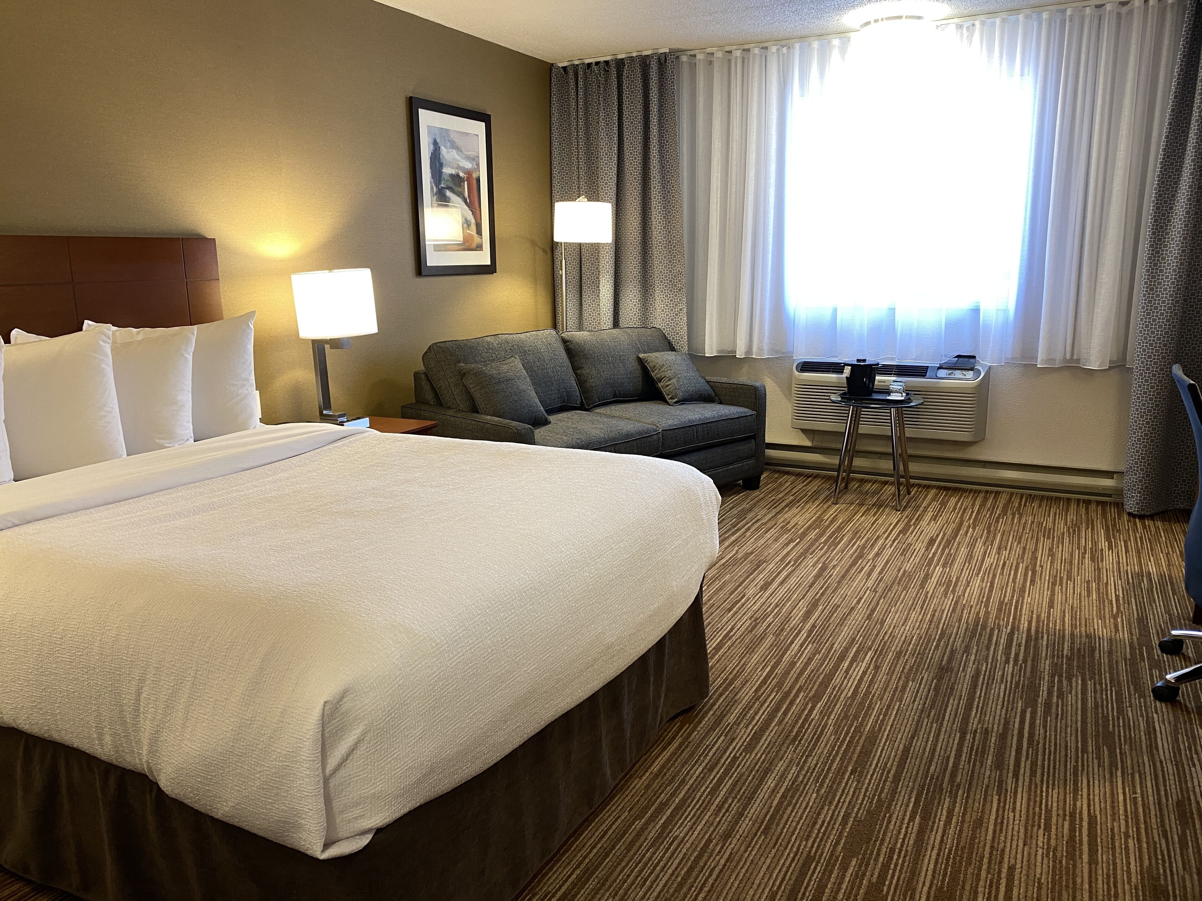 A hotel room with a large bed, a sofa, a desk, and a window with curtains.