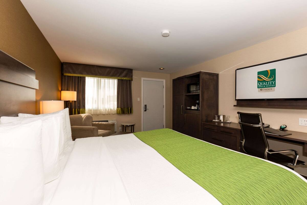A hotel room with a bed, a desk, a chair, a lamp, a television, and a door.