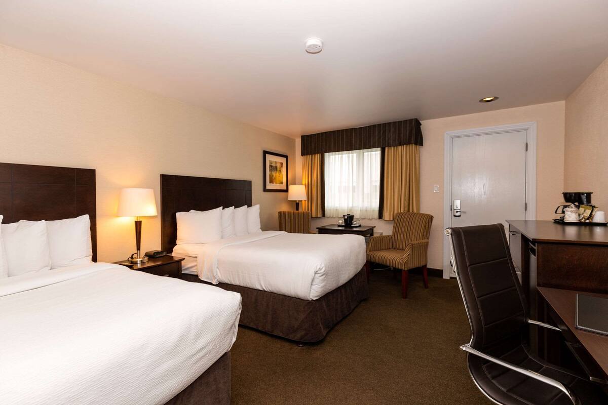 A hotel room with two beds, a desk, a chair, a lamp, a picture on the wall, and a door.