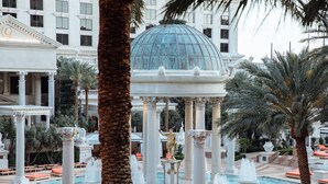 Une cour d’hôtel luxueuse, agrémentée d’une fontaine centrale, de palmiers et d’une architecture classique.