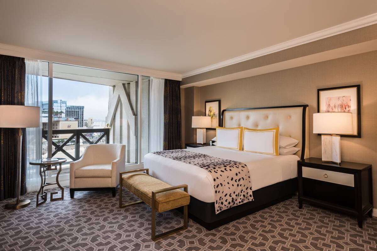 Une chambre d’hôtel avec un grand lit, une chaise, un banc, une table de chevet et une vue sur la ville.