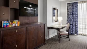 Habitación de hotel con un mueble de madera oscura, un televisor de pantalla plana, un escritorio con una silla y una cortina estampada.
