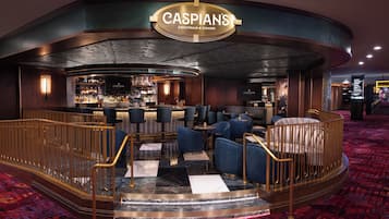 En bardel med en skylt som visar texten ”CASPIANS COCKTAILS & CAVIAR”, en bardisk, sittplatser med blå klädda stolar och en mönstrad matta.