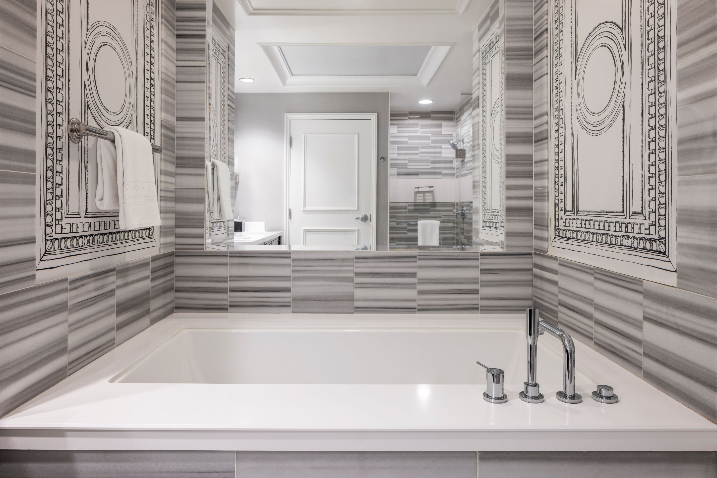 A modern bathroom with a large bathtub, a mirror, and a door leading to another room.