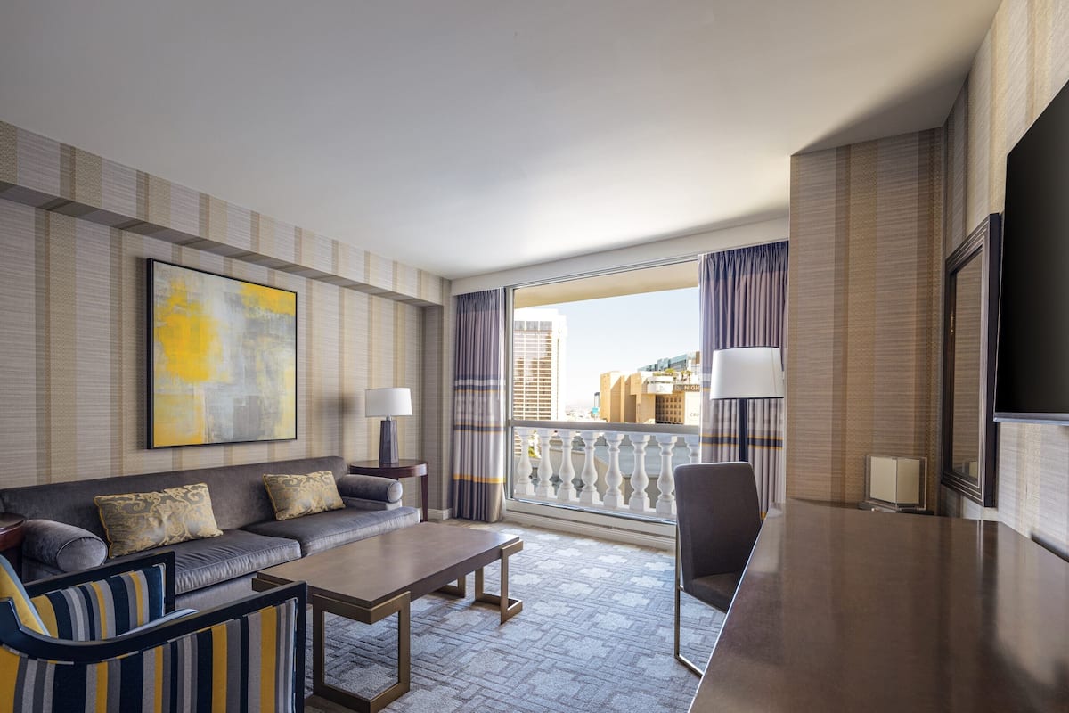 Une chambre d’hôtel avec un canapé, des fauteuils, une table basse, une télévision et un balcon avec des rideaux.