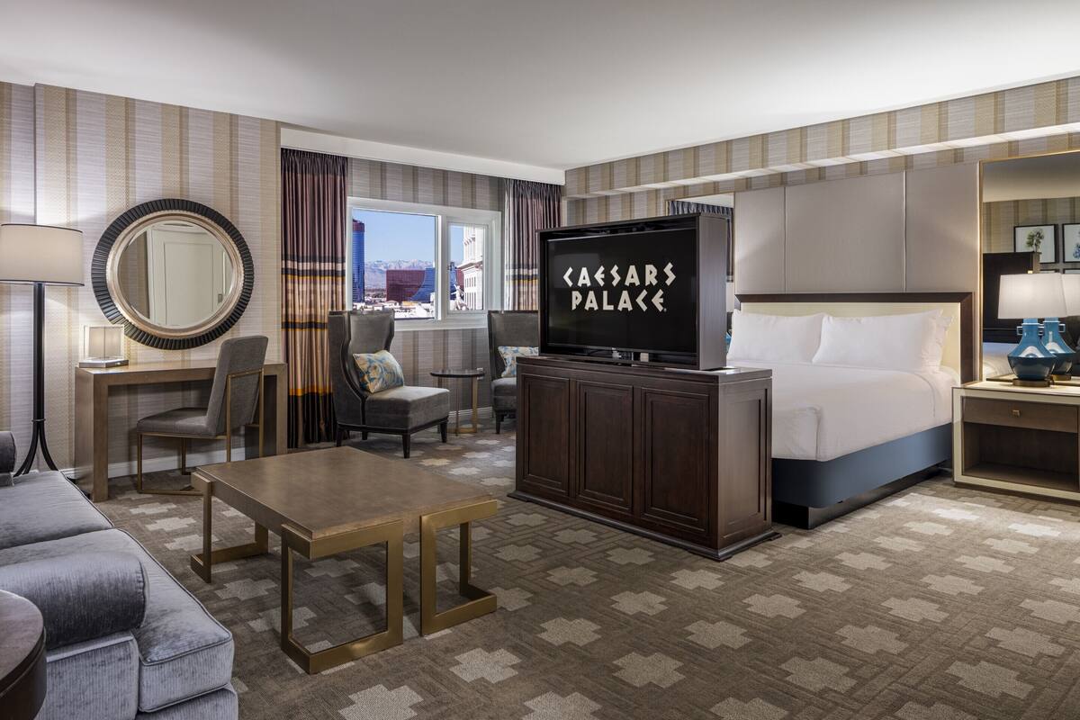 Une chambre d’hôtel équipée d’un lit, d’une télévision, d’un bureau, d’une chaise, d’un canapé et offrant une vue sur la ville.