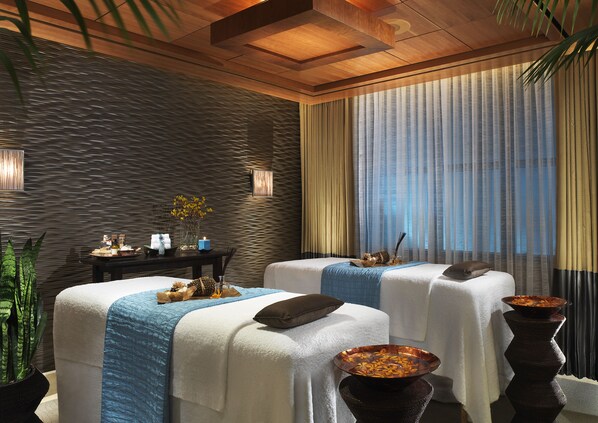 A spa room with two massage tables, a dark textured wall, a wooden ceiling, and a large window with sheer curtains. - Caesars Palace (Las Vegas)