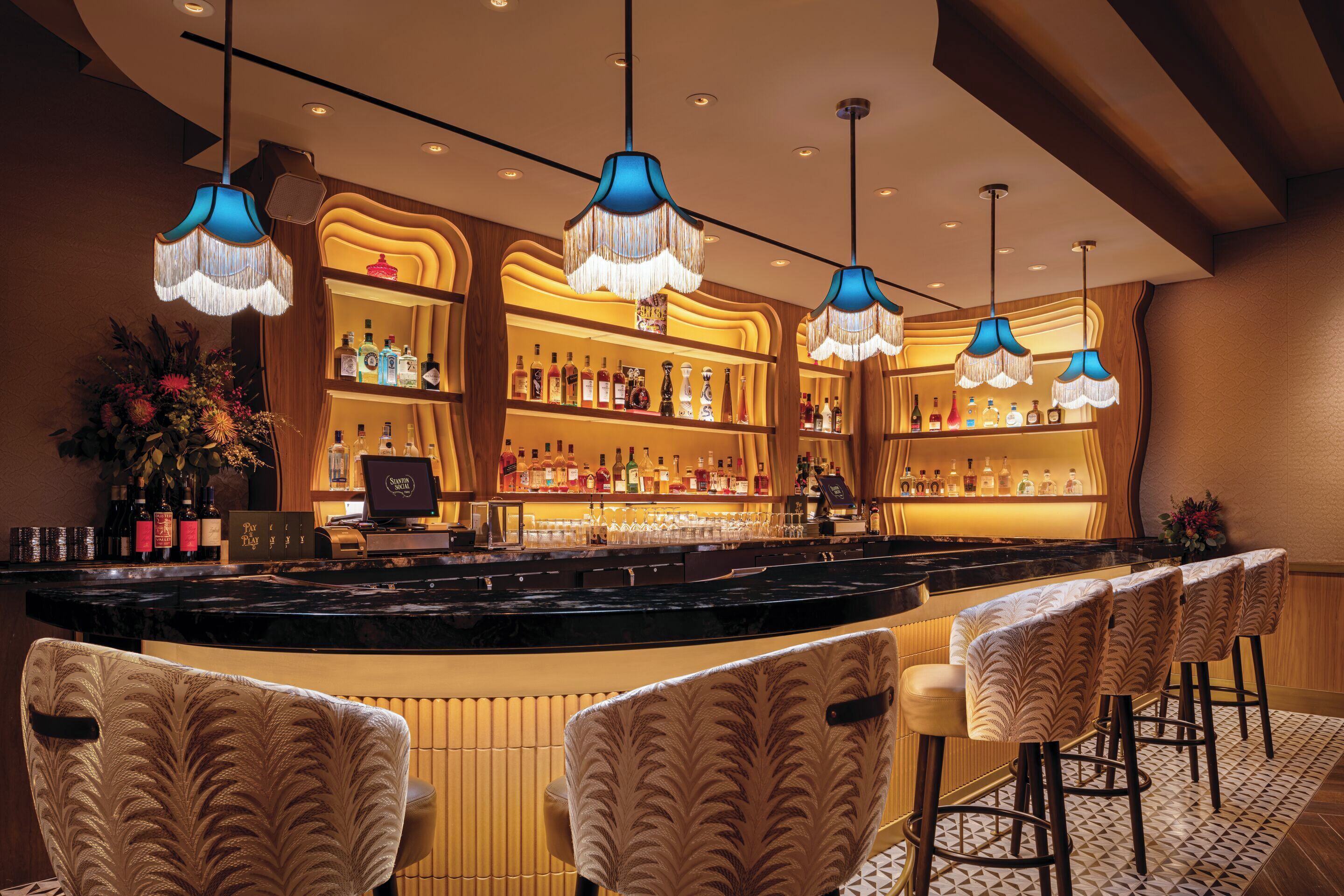 A bar area with a counter, bar stools, and hanging lamps.
