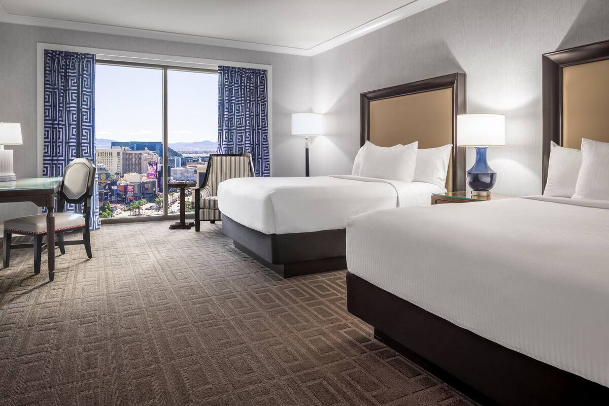 Une chambre d’hôtel avec deux lits, un bureau, une chaise, une lampe et une vue sur le paysage urbain.
