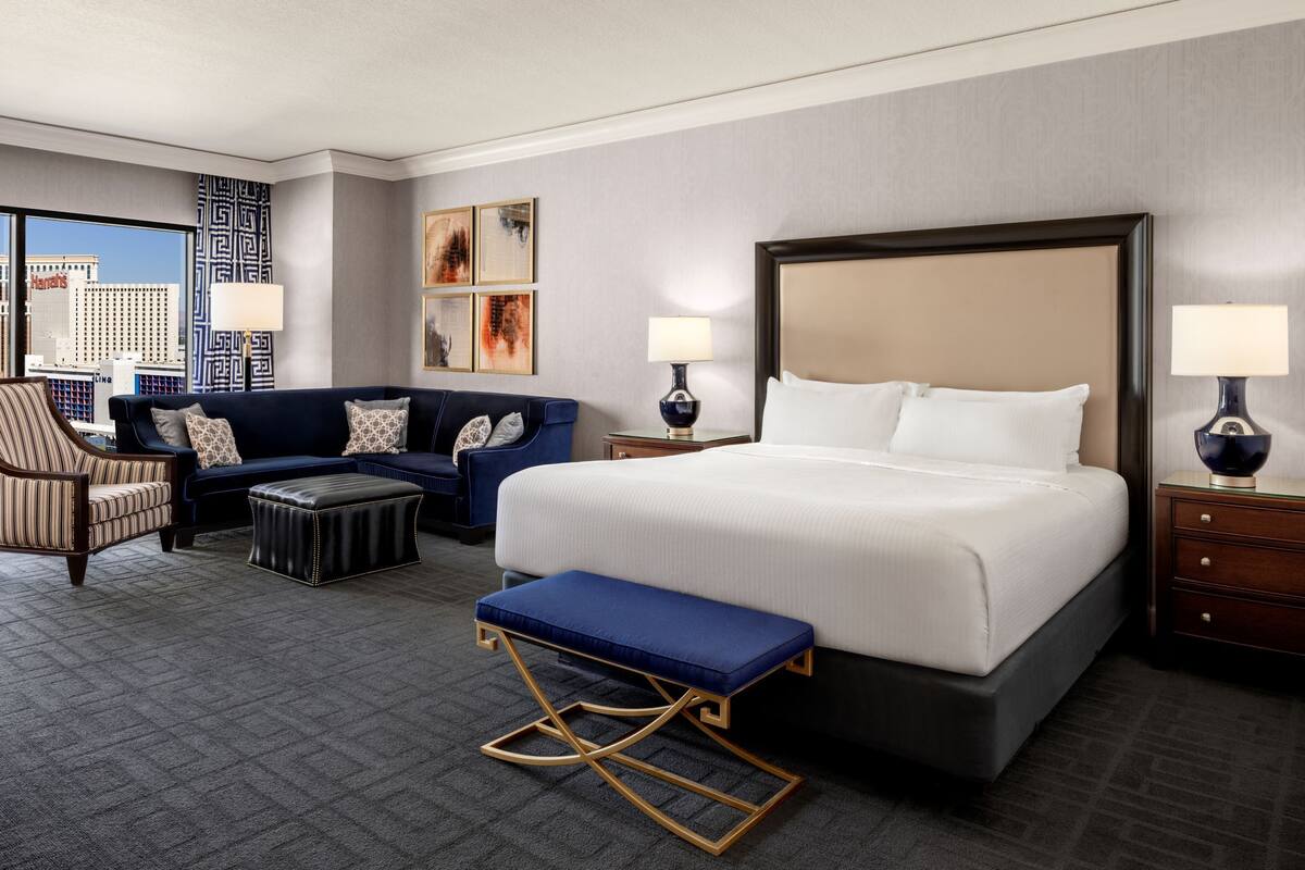 Une chambre d’hôtel avec un grand lit, un canapé, une chaise, un banc et une table de chevet avec des lampes.