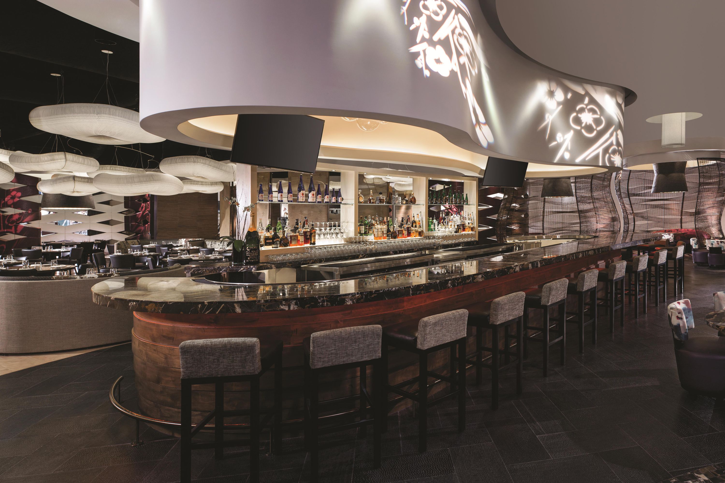 A modern bar area with a curved counter, multiple hanging light fixtures, and bar stools.