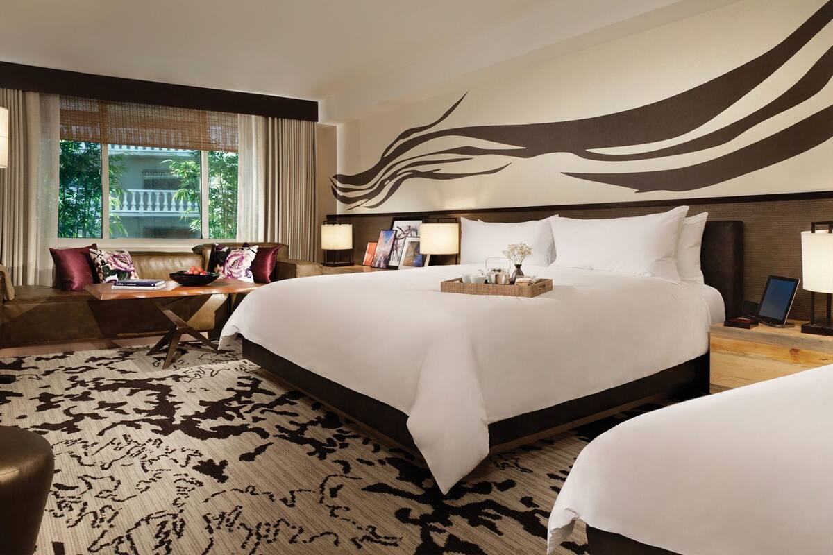 Une chambre d’hôtel avec un grand lit, un bureau équipé d’un ordinateur, une chaise et une vue sur la verdure.
