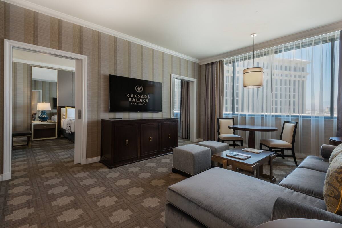 Une chambre d’hôtel dotée d’un grand téléviseur à écran plat fixé au mur, d’un canapé, d’une table basse et d’un coin repas avec des chaises.