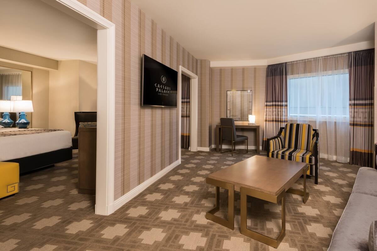 Une chambre d’hôtel avec un lit, un bureau, une chaise, un canapé et un téléviseur fixé au mur.