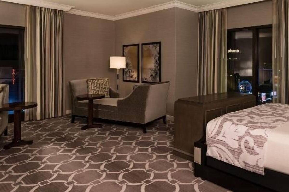 Une chambre d’hôtel avec un lit, un canapé, une chaise, une petite table et une lampe.